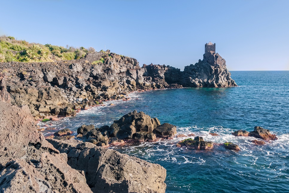 Rocky coastline of lava cliff near Acireale (Sicily), with a watchtower in the background