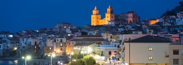 Cefalu, Italy - September 19, 2014: View at a parking with people and cars passing by the coast road during a warm summer evening near the old town of Cefalu, Sicily.