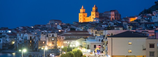 Cefalu, Italy - September 19, 2014: View at a parking with people and cars passing by the coast road during a warm summer evening near the old town of Cefalu, Sicily.