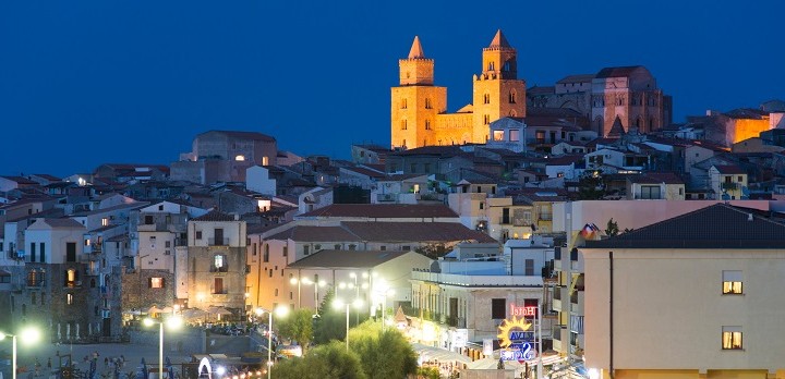 Cefalu, Italy - September 19, 2014: View at a parking with people and cars passing by the coast road during a warm summer evening near the old town of Cefalu, Sicily.